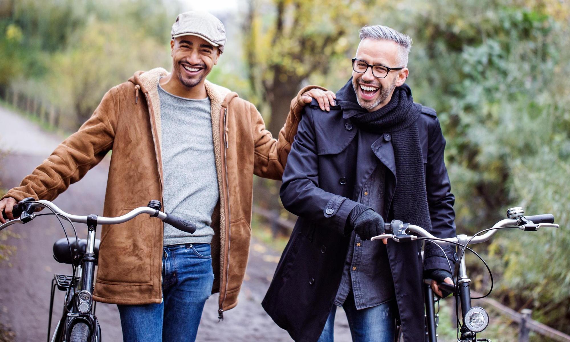Mid adult men laughing while walking with bicycles.