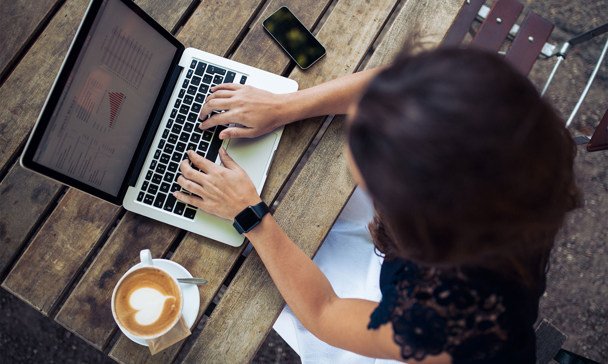 Kvinna sitter ute med en kaffe latte vid ett bord och jobbar på sin laptop